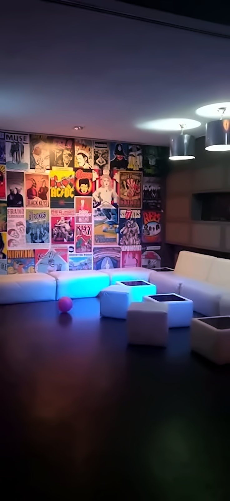 Zona de sofás blancos con mesas iluminadas junto a la pared de carteles